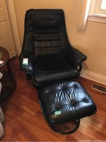 Front angled view of black faux leather chair and ottoman showing cushions, armrests, and swivel bases.