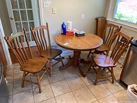 Photo showing four wooden dining chairs around a small round wooden table in a tiled kitchen area. Chairs have spindle backs and turned legs.