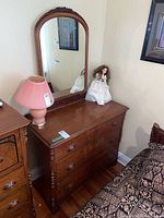 Full front view of the wooden dresser with attached mirror showing lamp and doll on top.