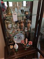 Photo showing brass and glass bells on shelf with various ceramic vases and figurines below