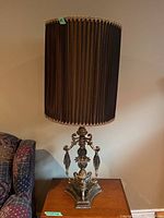 Photo showing full view of one ornate table lamp with pleated fabric shade and metal/crystal base on wooden table.