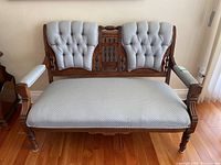 Front view of the Victorian style loveseat with carved wood frame and light blue patterned upholstery, showing tufted back cushions.