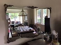 Rectangular wall mirror with dark frame and ornate metal corner decorations, photographed hanging on wall reflecting a dining room.