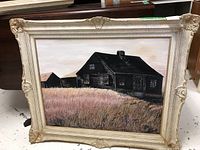 Framed original oil on board painting of rustic houses in a field with visible frame damage.