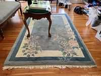 Full view of the rectangular area rug with floral design placed on wooden floor, partially under a glass-top table.