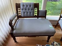 Victorian style settee with wooden carved frame, upholstered seat and back with button tufting and diamond-pattern fabric upholstery in light gray.