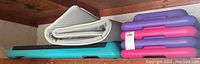 Exercise stepper and folded exercise mat stacked together on a shelf.