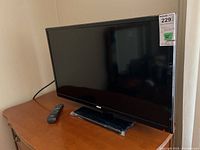 Front view of the RCA 32 inch television with remote control resting on a wooden surface.