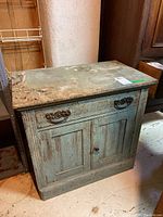 Front view of the small vintage wooden cabinet showing two panel doors, drawer, and worn crackled blue paint.