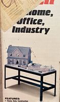 Photo showing a heavy duty work bench with a dark metal frame and a rectangular work surface, displayed with small objects including model houses.