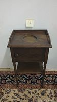 Front view of the wooden humidor cabinet against a wall, on a patterned rug, showing the overall structure with top tray, door, turned legs, and lower shelf.