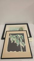 Two framed lithographs, one depicting botanical leaves on dark background, the other a Paris Eiffel Tower scene, both signed and numbered.