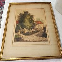 Framed hand colored engraving featuring a rustic homestead with stone buildings, greenery and a dirt path. Signed in pencil at the bottom right.