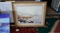 Framed watercolor painting of a coastal shoreline showing rocks, grasses, and lighthouses in the distance.