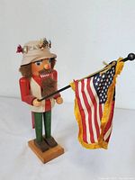 Full view of wooden nutcracker holding a fringed American flag replacing the fishing pole.