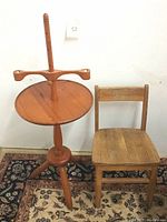 Photo shows vintage maple wood candle holder stand with round top and peg adjustments alongside vintage oak child's school chair on patterned carpet.