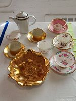 Overview of various vintage porcelain and ceramic pieces including teacups, saucers, coffee pot, creamers, and golden bowl