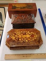 Top-down view of three vintage jewelry boxes showing cedar box with painting, carved wood box, and lacquered music box with floral design.