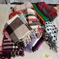 Multiple wool cashmere scarves in various colors and patterns laid on white surface with number 34 tag visible