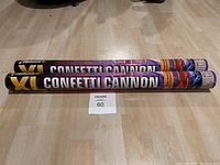 Two XL confetti cannons laid side by side on a light wood floor showing full length and branding.