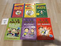 Photo shows six Big Nate comic books laid out on a wooden surface. Covers feature colorful cartoon illustrations and titles.