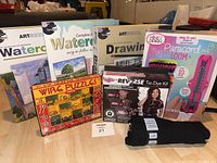 Full lot overview showing all arts and crafts items: 2 watercolor sets, 1 drawing set, paracord loom kit, tie-dye kit with black youth large T-shirt, and wire puzzle kit arranged on floor