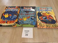 Photo of three Bird & Squirrel graphic novels laid flat on wood surface side by side: On Fire, All Tangled Up, All Or Nothing.