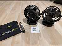 Two black Opolar clip fans and Goal Zero Nomad 35 solar power pack with USB cylinder on light wooden floor