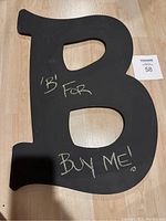 Photo of the black chalkboard letter B with chalk writing 'B for Buy Me!' visible on the surface.