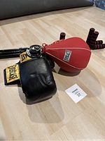 Photo of black and yellow Everlast sparring gloves and red Everlast punching bag on floor