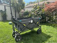 Side and handle view of folding utility wagon on grass showing metal frame, fabric sides and wheels