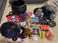Photo of Halloween party lot including black cauldron, red skull bag, fake spider webs with spiders, packaged themed napkins and plates, tinsel curtains, skeleton disco ball with some missing mirrored tiles, and various small packaged items