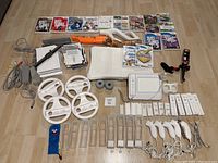 Overview of two Wii consoles, multiple controllers, attachments and game cases laid out on floor