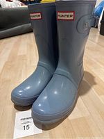 Front angled view of pair of women's Hunter rain boots in cornflower blue, showing full height and wear marks on boots