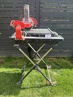 Full view of Husky tile saw mounted on foldable stand on grass with black fence background.