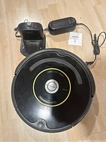 Top view of black Roomba robotic vacuum with charging dock and power adapter on wood floor