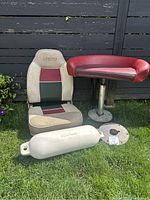 Two Legend boat seats and a white boat bumper placed outdoors against a black fence on grass. Items show dirt and weathering.