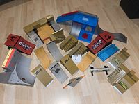 Top down view of array of Tech Deck ramps and rails arranged on light wood flooring, showing multiple ramp shapes including quarter pipes, stairs and launch ramps with various logos and stickers.