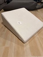 Overall angled view of the white memory foam wedge pillow showing the fabric texture and incline shape on a wood floor.