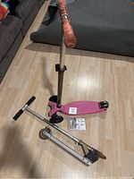 Photo of two scooters on wooden floor; one pink Maxi-Micro scooter and one silver foldable Razor scooter with visible weathering and wear.