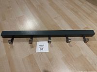 Front view of the grey wall-mounted rack with 5 silver metal hooks displayed flat on wood floor.