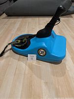 Blue Zipfy Freestyle Mini Luge sled with attached black joystick steering handle, side view showing '08' decal and bungee tether cord attached for pulling or control.