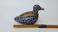 Side view of porcelain and brass duck figurine approximately 6 inches in length with visible ruler for scale.