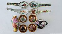 Top-down view of four decorated porcelain spoons, four small plates, one floral vase, and one black floral pot with lid.