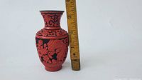 Front view of red lacquer carved vase with floral and scroll motifs, showing height next to ruler.