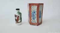 Handpainted glass snuff bottle with rooster design and porcelain brush holder with floral motifs side by side on white background.