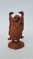 Front view of the wooden carved Buddha figurine, showing the smiling, joyful expression and raised arms.