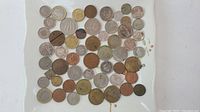 Top view of a plate with around 40 assorted coins from various countries, varying in size and color from silver, bronze, to gold-toned metals.