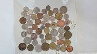 A display of 50 assorted coins from multiple countries, showing various sizes and colors including silver, bronze, and gold tones, arranged in loose rows on a white background.