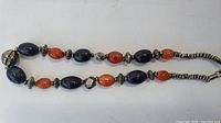 Full view of the multi-colored gemstone necklace with dark blue and reddish-orange beads and silver-toned spacers